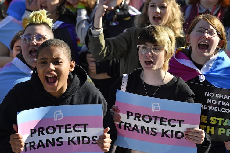 Trans youth holding signs reading 'PROTECT TRANS KIDS'