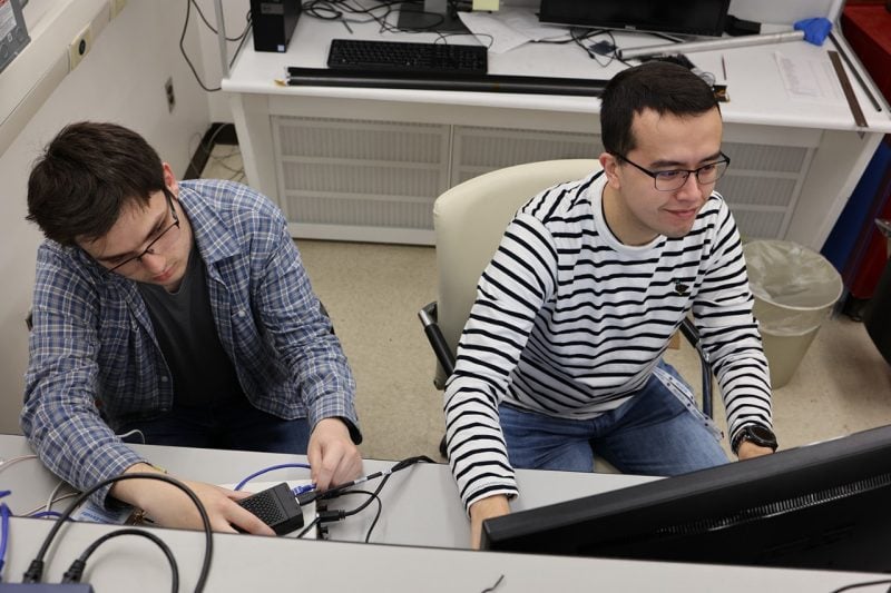 Undergraduate Thomas Wheeler (at left) and Ph.D. candidate Bruce Barbour work on the hardware-in-the-loop test bed that emulates the changing connectivity of a mega-constellation at scale.