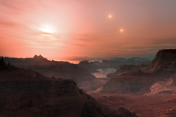 An artist’s impression of sunset on an austere exoplanetary landscape, in this case of the super-Earth Gliese 667 Cc. The exoplanet resides in a triple star system and the three suns are visible in the sky. 