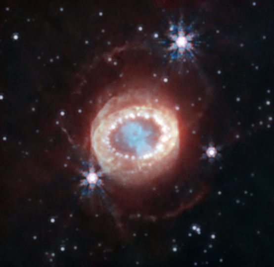 Webb’s NIRCam (Near-Infrared Camera) captured this detailed image of SN 1987A (Supernova 1987A). At the center, material ejected from the supernova forms a keyhole shape. Just to its left and right are faint crescents newly discovered by Webb. Beyond them an equatorial ring, formed from material ejected tens of thousands of years before the supernova explosion, contains bright hot spots. Exterior to that is diffuse emission and two faint outer rings. In this image blue represents light at 1.5 microns (F150W), cyan 1.64 and 2.0 microns (F164N, F200W), yellow 3.23 microns (F323N), orange 4.05 microns (F405N), and red 4.44 microns (F444W). 