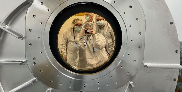 SPHEREx team members can be seen in a reflection from the chamber's gold-coated, sapphire window. The window protects the telescope inside the chamber from the infrared glow of the lab outside. Clockwise from top are Stephen Padin, Phil Korngut, Chi Nguyen, and Howard Hui.