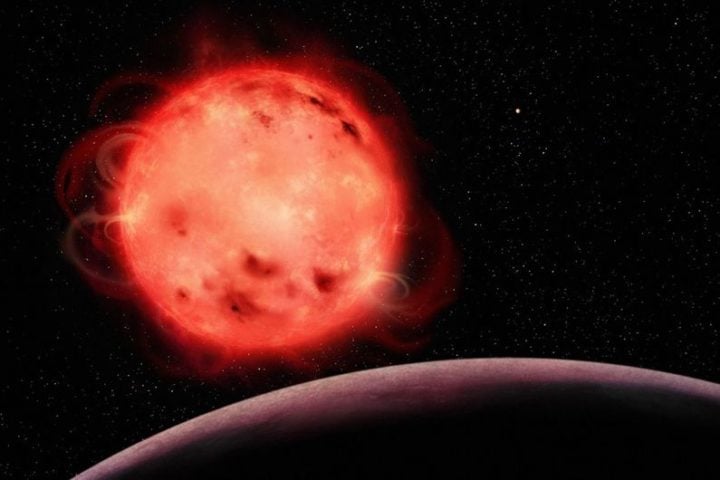 This artistic representation of the TRAPPIST-1 red dwarf star showcases its very active nature. The star appears to have many stellar spots (colder regions of its surface, similar to sunspots) and flares. The exoplanet TRAPPIST-1 b, the closest planet to the system’s central star, can be seen in the foreground with no apparent atmosphere. The exoplanet TRAPPIST-1 g, one of the planets in the system’s habitable zone, can be seen in the background to the right of the star. The TRAPPIST-1 system contains seven Earth-sized exoplanets. 