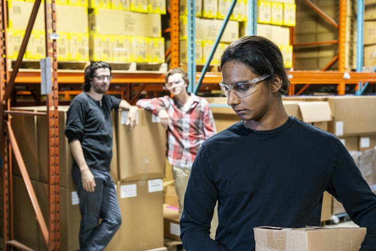 worker in foreground aware of two in background of warehouse scene, watching