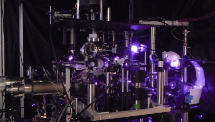 The purple glow of an infrared laser illuminates the optical bench used in the experiment. The laser is used to precisely control the quantum states of cesium atoms in a vacuum chamber. 