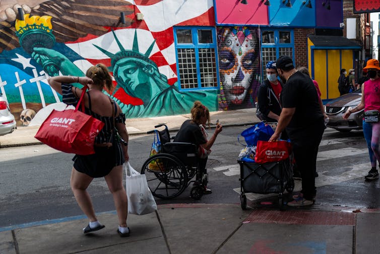 People on an urban street corner gather their belongings on front of colorful murals