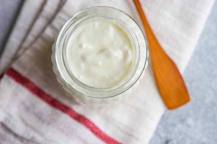 Jar of yogurt and a wooden spoon on a towel