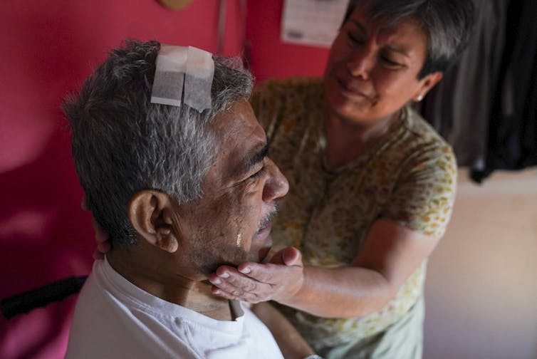 A woman doctors a man with a bandage on his head.