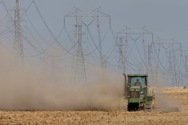 Dust billows as a farmer plows a dry field on a tractor.