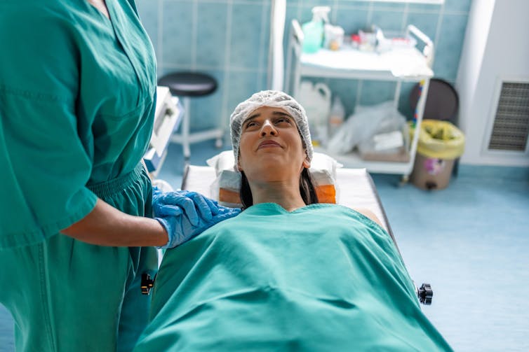 Patient lying on operating table under blanket, smiling up at provider