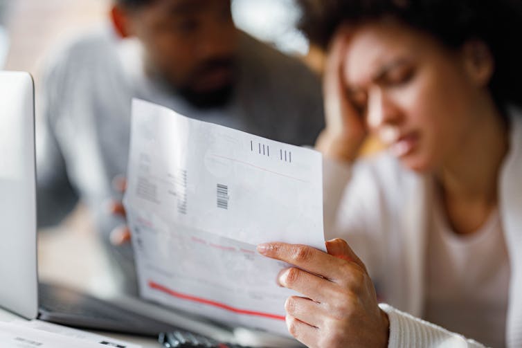 Person with head in hand in front of laptop, holding medical bill as another person looks on with them