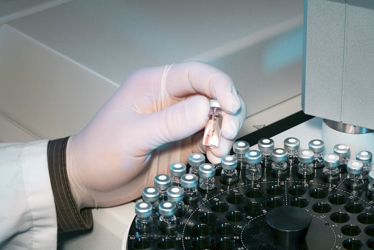 Gloved hand picking up vaccine vial among a tray of vaccine vials