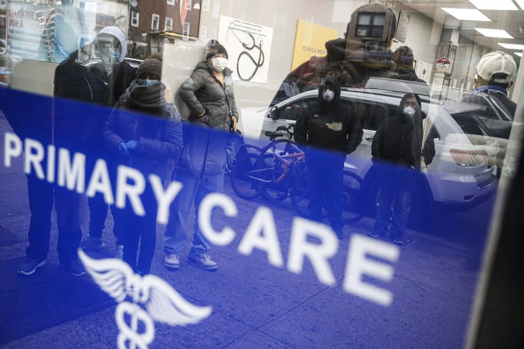 Glass wall of primary care clinic, reflections of people outside the building looking at people on the inside