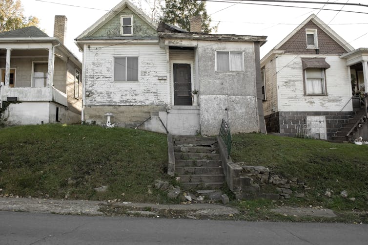 Three run-down houses with peeling paint on a street.