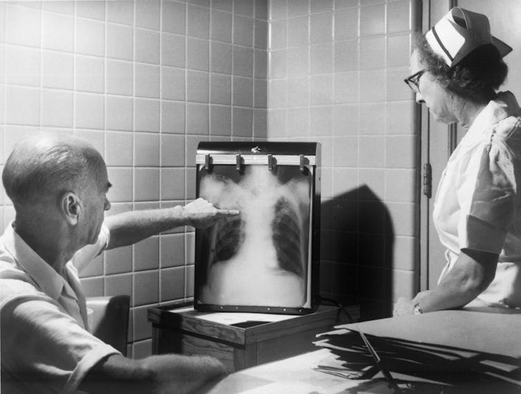 An historical photo of a doctor and nurse examining a TB-positive X-ray.