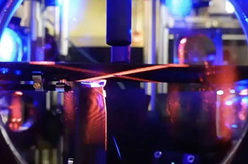 The team's experimental setup: Atoms are cooled and slowed inside a vacuum chamber, until they can be trapped in a lattice inside a cavity (black triangular cavity spacer in the bottom half of the vacuum chamber.) Fluorescence of the atoms can be seen on top in blue from hot atoms interacting with the Zeeman slower laser, and in a thin strip in the lower half from atoms trapped inside the cavity. Credit: JKT/ZN Study demonstrates continuous recoil-driven lasing using laser-cooled strontium atoms