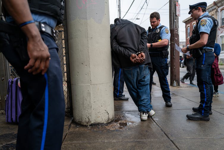 A man in handcuffs facing away from the camera is being arrested by two police officers.