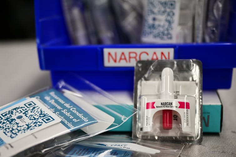 A white bottle of naloxone in a package sits in front of a blue bin.