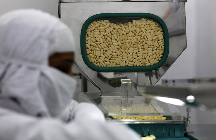 Person in protective covering watches a large batch of pills coming out of a machine