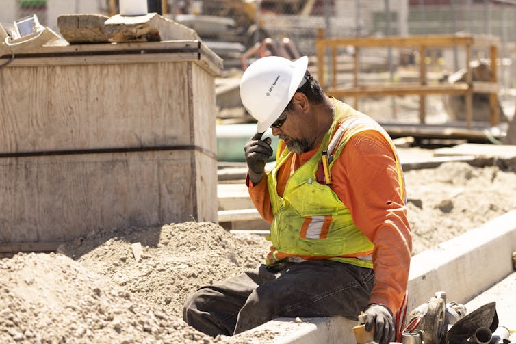 A construction worker sits and puts his head down, still in the hot sun.
