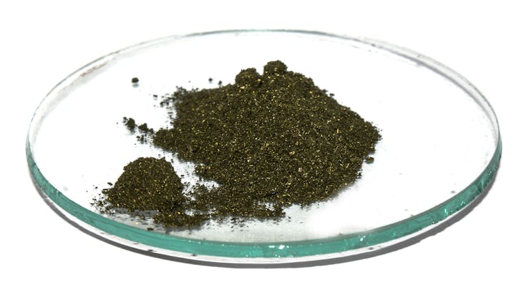 A glass dish holding a small mound of dark green crystalline powder