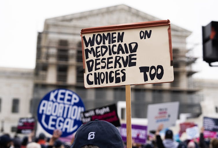 A protester holds a sign aloft that says 'Women on Medicaid deserve choices too,' with another sign in the background that says 'Keep Abortion Legal,'