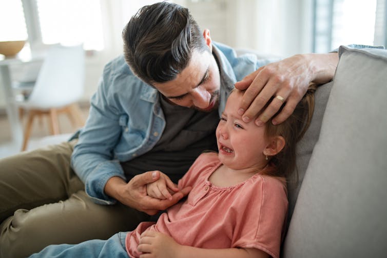 A father consoles his young daughter as she cries.