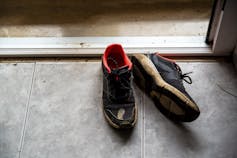 A worn pair of running shoes sit just inside a door frame