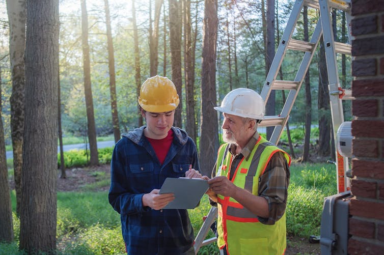 A young man gets guidance from an older worker at a construction site.