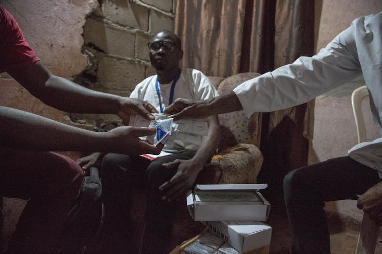 Arm of doctor handing condom and lubricant to a patient, with another person looking over