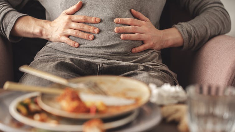 Person gripping stomach, stacked plates of mostly eaten food before them