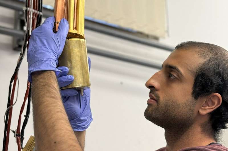 Ph.D. student Vivek Wadhia sets up the dilution fridge inside which the quantum clock experiment was carried out. Credit: Martyna Sienkiewicz. Reading a quantum clock costs more energy than running it, study finds