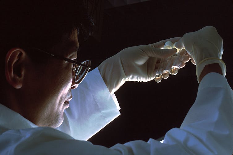 A scientist holds three test tubes in his gloved hands