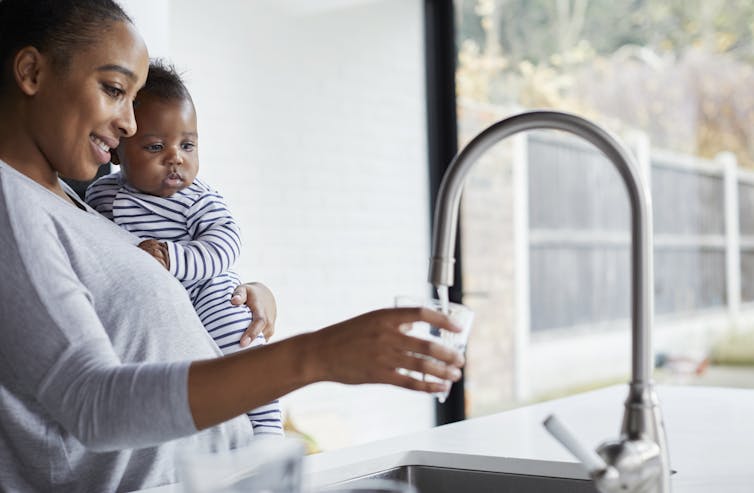 A woman holding a small child fills a glass with water.