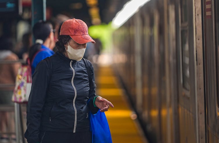 A woman wears a face mask to filter the air while standing on a subway platform.