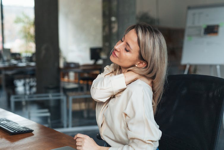 Middle-aged woman sitting near her computer, rubbing her neck.