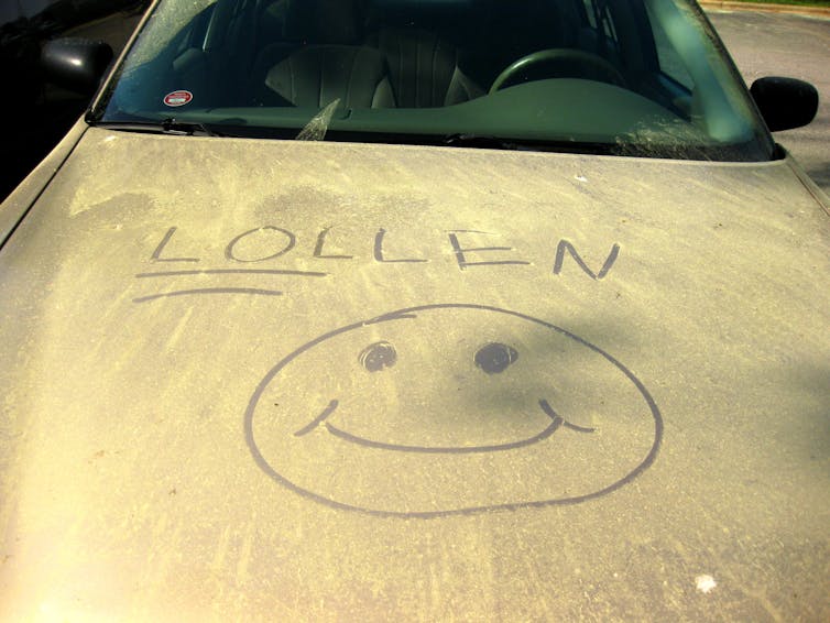 Someone drew a smiley face and the word Lollen on a car hood covered in yellow pollen grains.