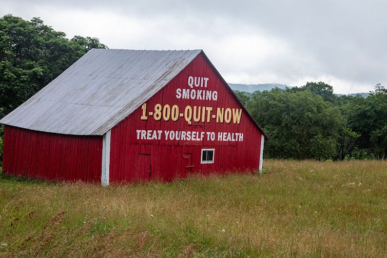 Red barn in a field with the words 'QUIT TOBACCO 1-800-QUIT-NOW TREAT YOURSELF TO HEALTH' painted on one side