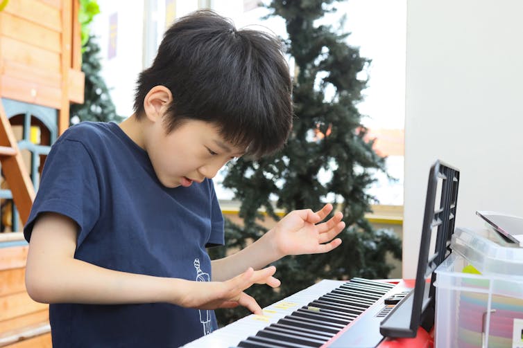 A young boy wearing a blue shirt presses on a key of a piano.