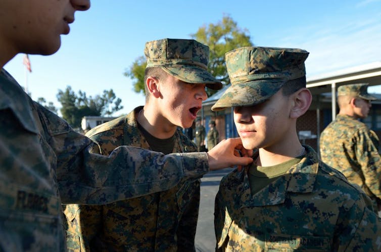 Boys in uniform standing outside, one with a hand on another's shoulder while another another's mouth is open
