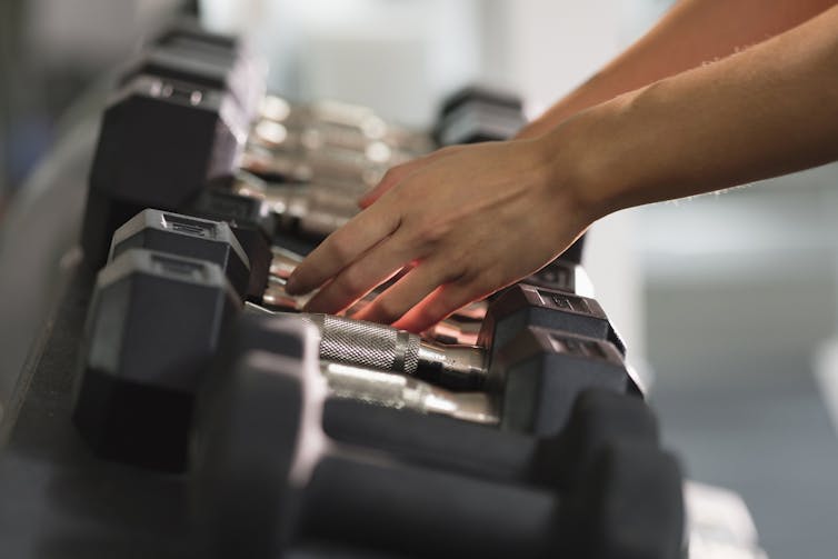 Person reaching towards dumbbells on a rack