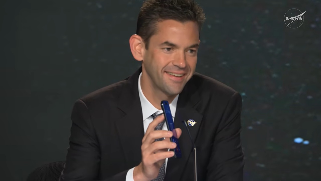Jared Isaacman holds a cell phone near a microphone.