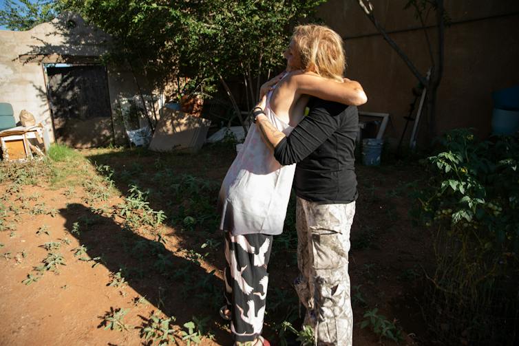 Two women hugging in a rural yard.